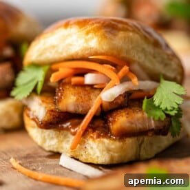 Close up: Fried Pork Belly Sliders on soft buns with thin slices of carrots and onions, garnished.