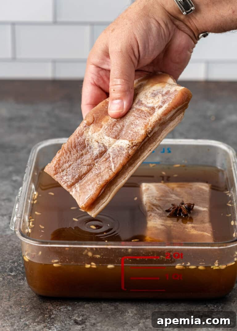 Carefully placing a raw pork belly slab into the prepared brining solution in a large container.