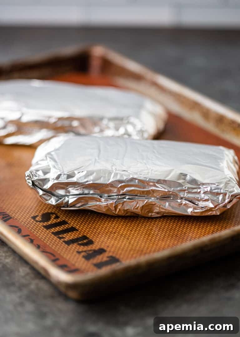 Foil-wrapped pork belly packets arranged on a baking sheet, ready for the oven.
