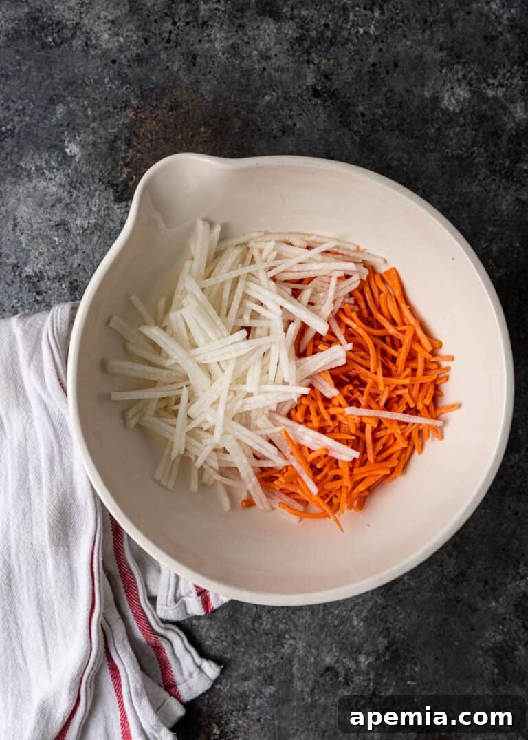 Overhead shot of julienned carrots and daikon radish in a white mixing bowl, pre-marination.