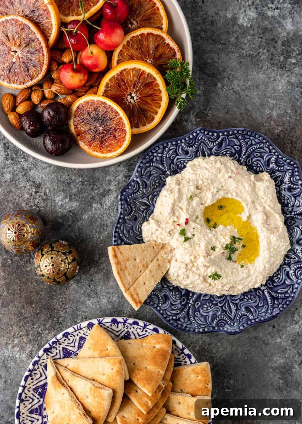 Fiery Feta Dip 3 overhead view of a table spread featuring separate bowls of fresh fruit, a blue bowl of creamy tyrokafteri, and triangles of pita bread