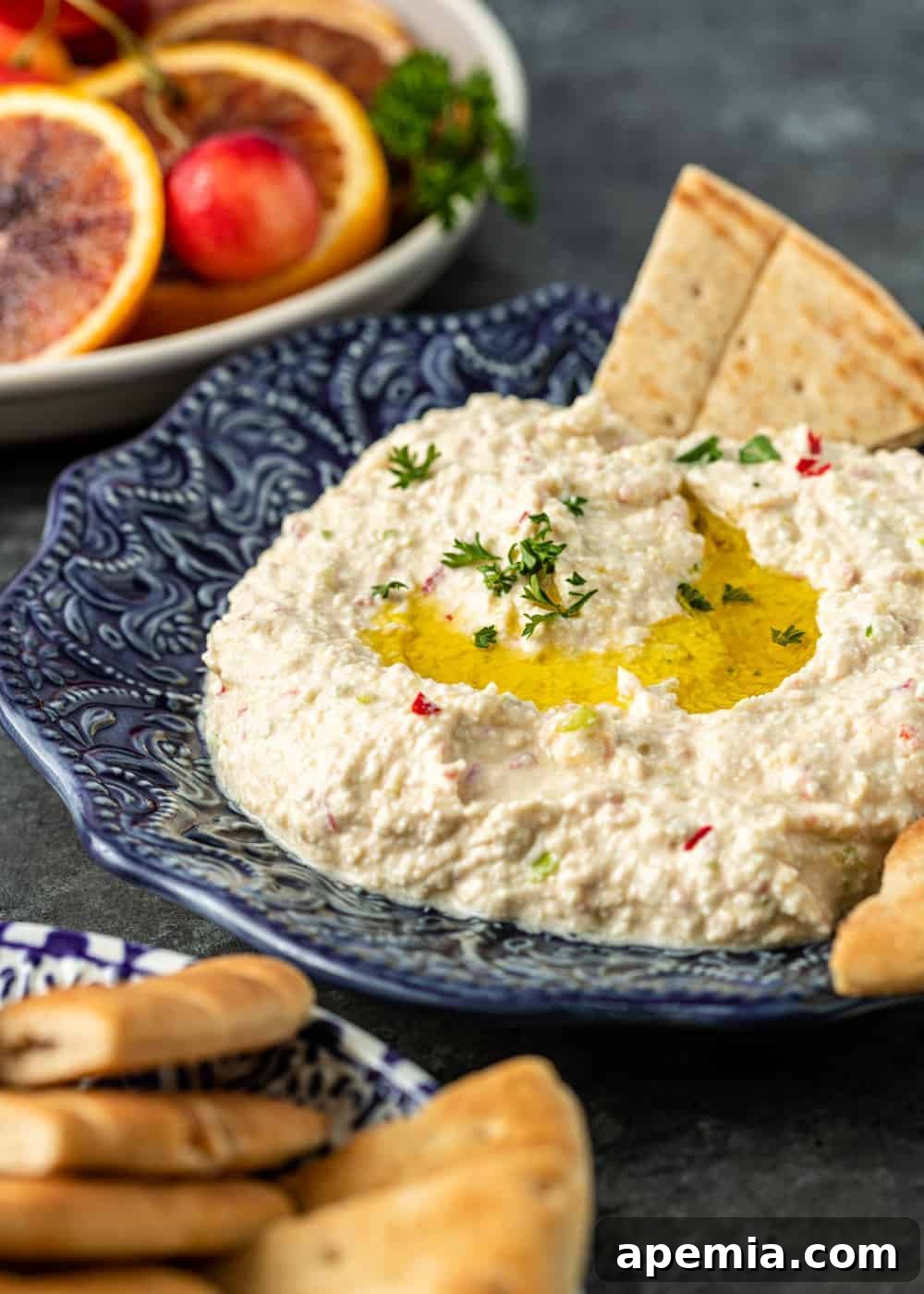 Fiery Feta Dip 4 side view closeup of a blue ornate bowl filled with creamy Tirokafteri, with fresh fruit and pita bread in the softly blurred background