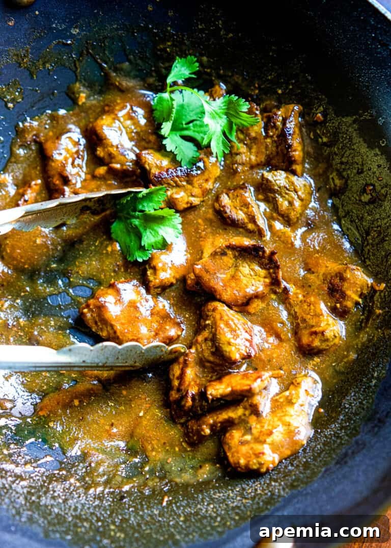 A close-up overhead shot of Chinese Beef Curry being stirred in a wok with tongs, highlighting the rich sauce and tender meat.