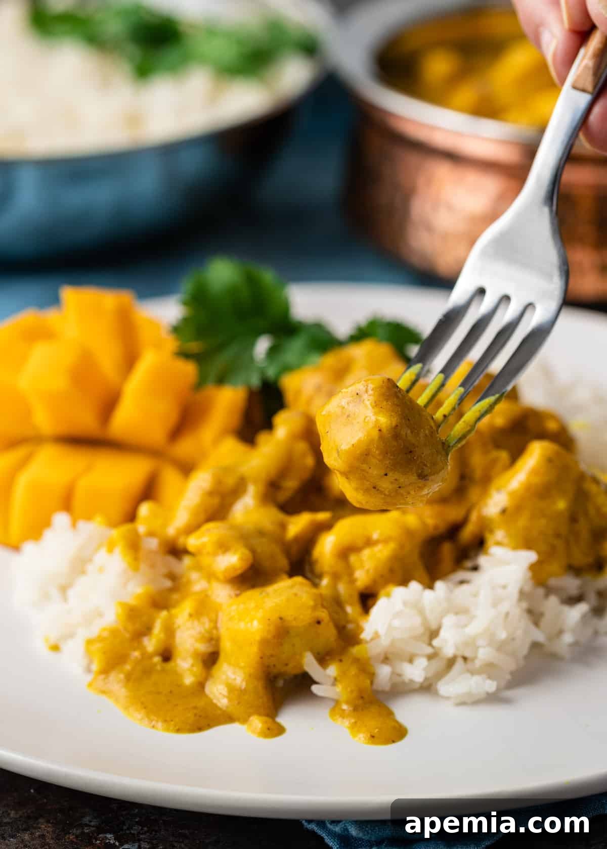 A fork holding a piece of tender yellow mango chicken curry, inviting a taste