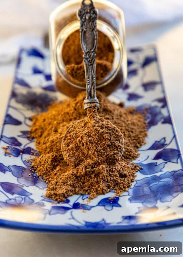 Spoonful of ground spices balanced against a spice jar on a blue and white plate, highlighting the rich color.