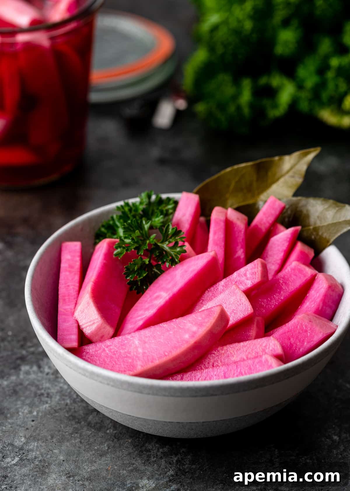 Close-up shot of perfectly pink pickled turnips, neatly sliced in a small white bowl, ready to be served.