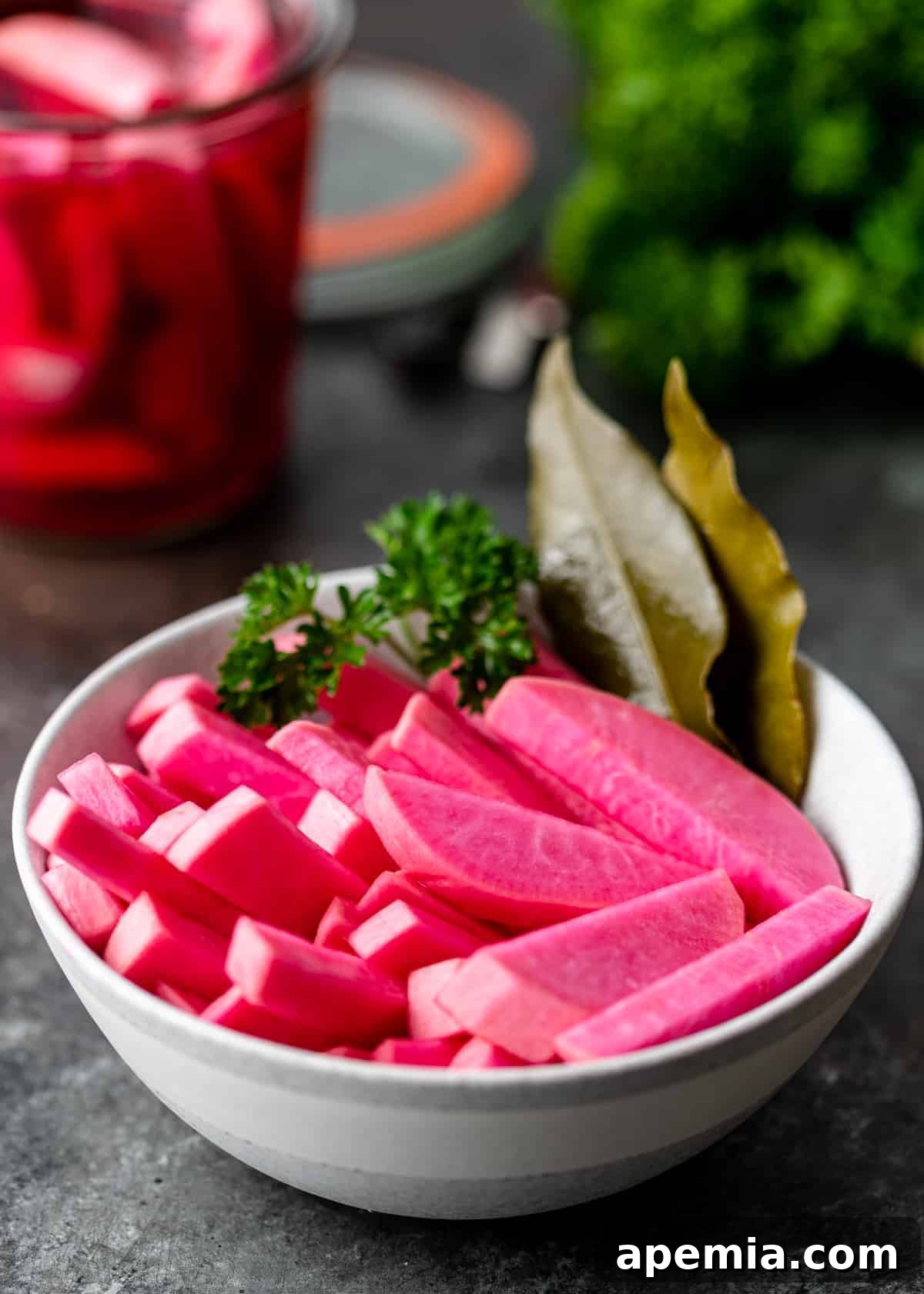 A white bowl filled with my homemade pickled turnips, garnished with bay leaves and fresh herbs, showcasing their beautiful pink color.