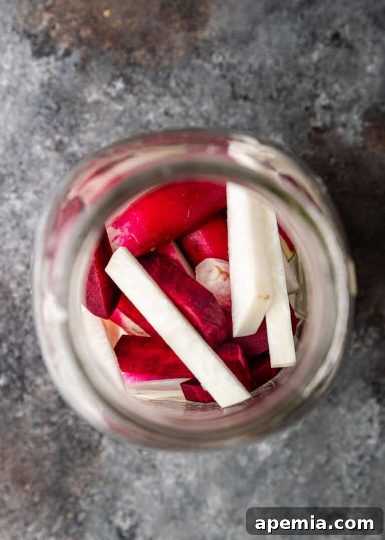 Overhead close-up of a mason jar filled with red and white root vegetables, before the pickling process begins.
