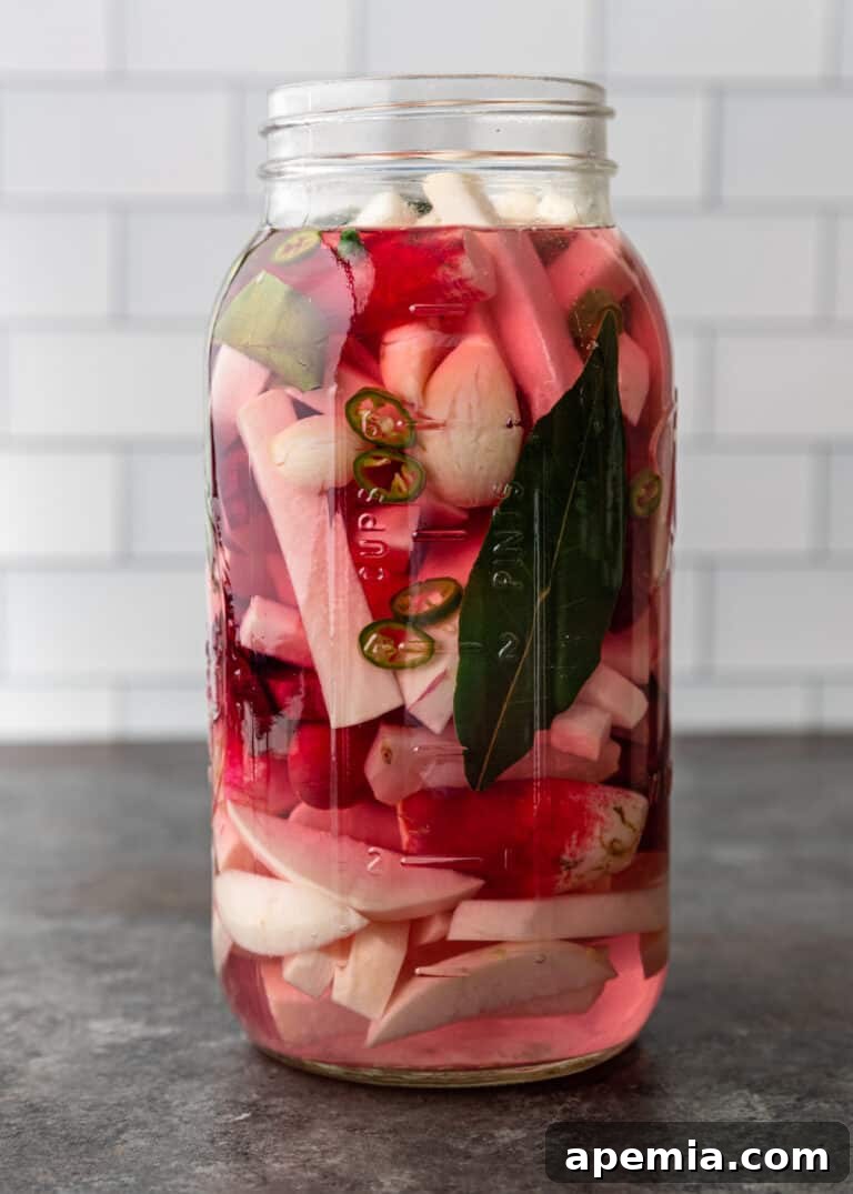 Side view of sliced green chiles and white root vegetables beginning to brine in a large mason jar on Day 1.