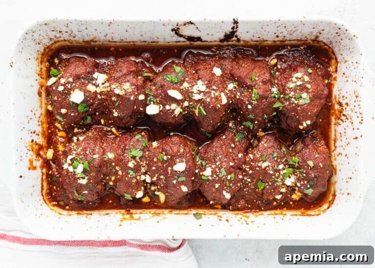 Soutzoukakia in a white casserole dish, simmering in their rich tomato sauce