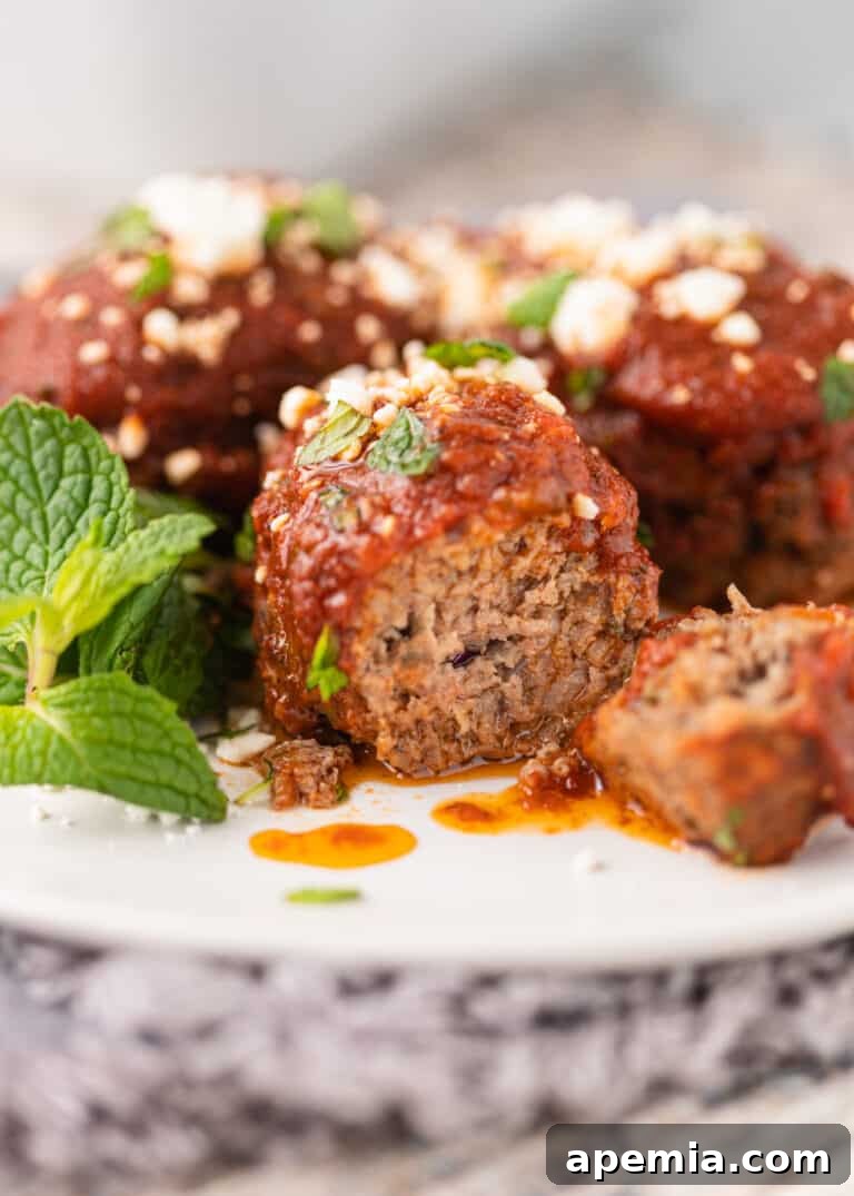 Greek beef meatballs on a white plate, with one sliced open to show its juicy interior