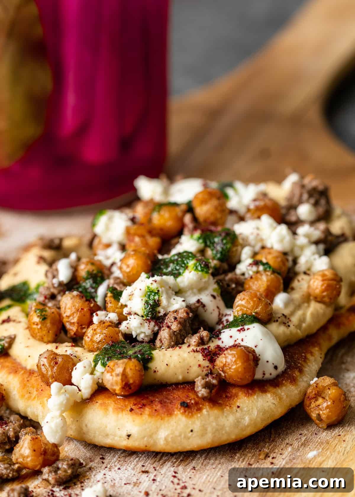 A perfectly cooked Mediterranean Flatbread Pizza, topped with spiced ground lamb and melted feta, resting on a wooden cutting board next to the skillet it was cooked in.