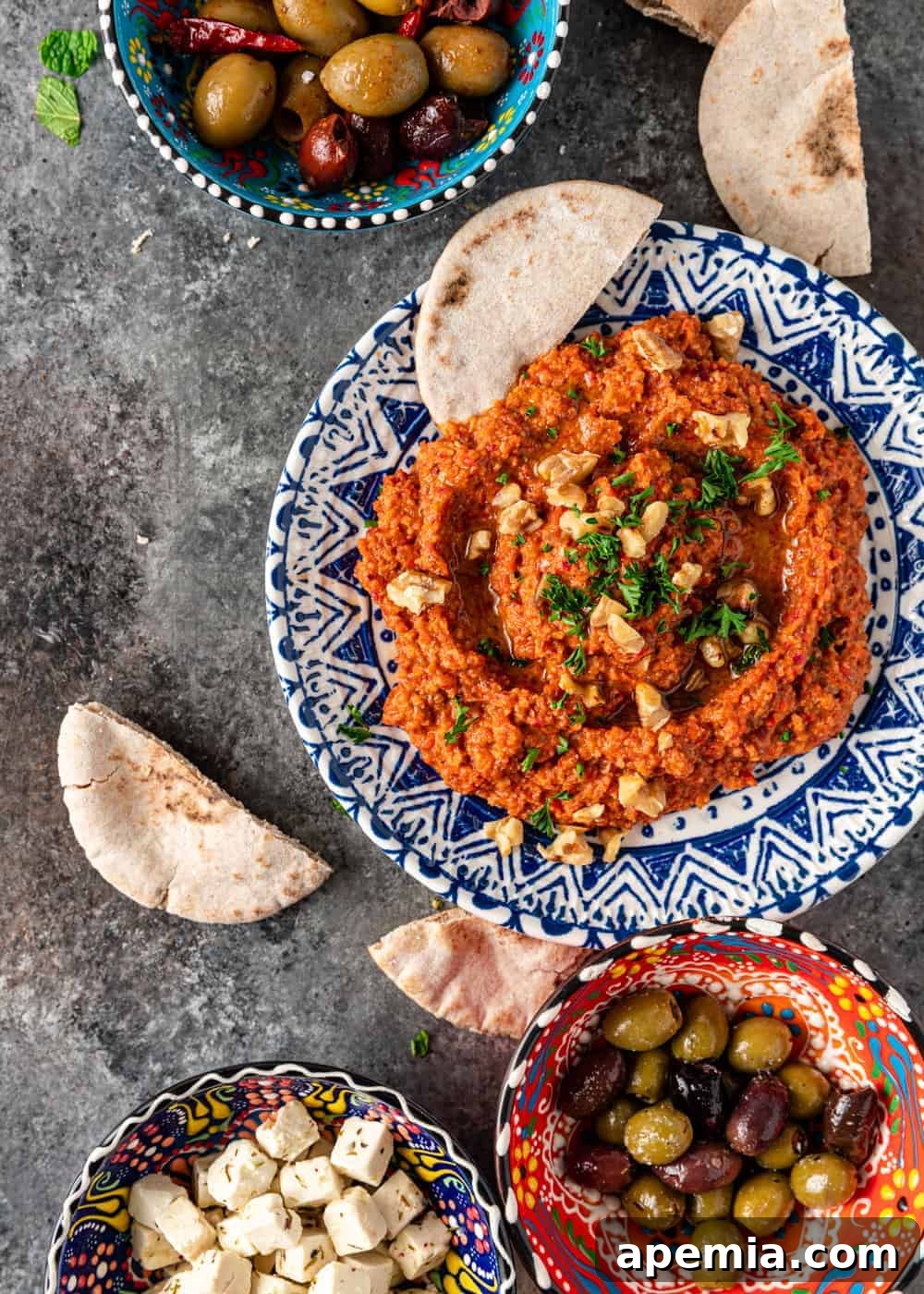 Muhammara: Mediterranean Red Pepper Walnut Dip 5 overhead: muhamara dip in blue bowl next to bowls of Greek olives and marinated feta cheese
