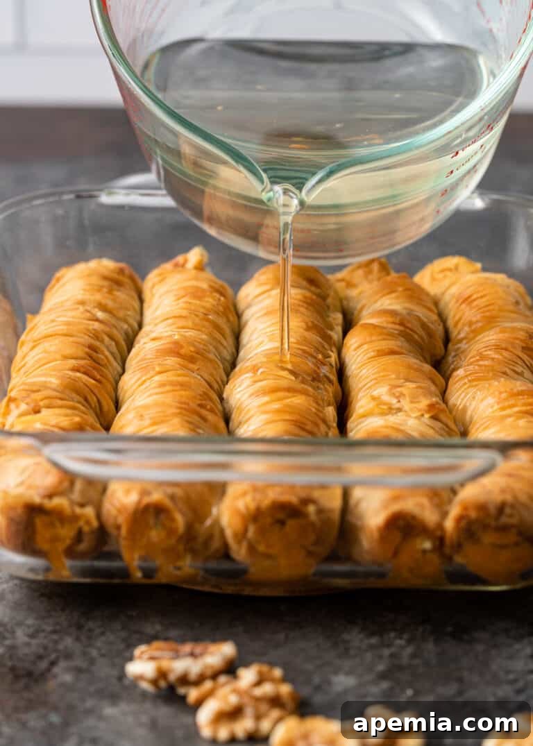 pouring sugar syrup over pan of baked Greek baklava rolls, creating a sweet glaze