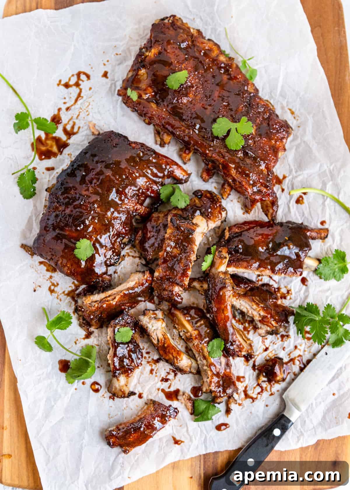 Overhead shot of sweet and sour ribs being cut apart on white parchment paper, showcasing their tenderness.