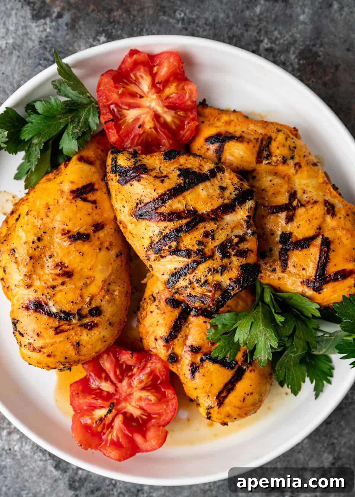 Overhead shot of grilled saffron chicken artfully arranged on a large platter, garnished with fresh tomatoes and sprigs of herbs.