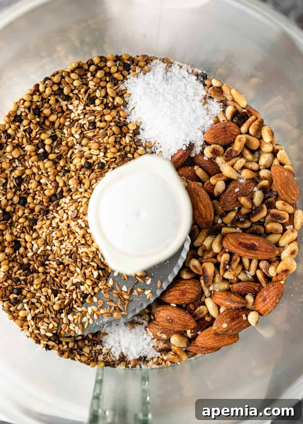 Overhead image: Assorted nuts, seeds, and spices waiting in the bowl of a food processor to be transformed into a homemade dukkah recipe.