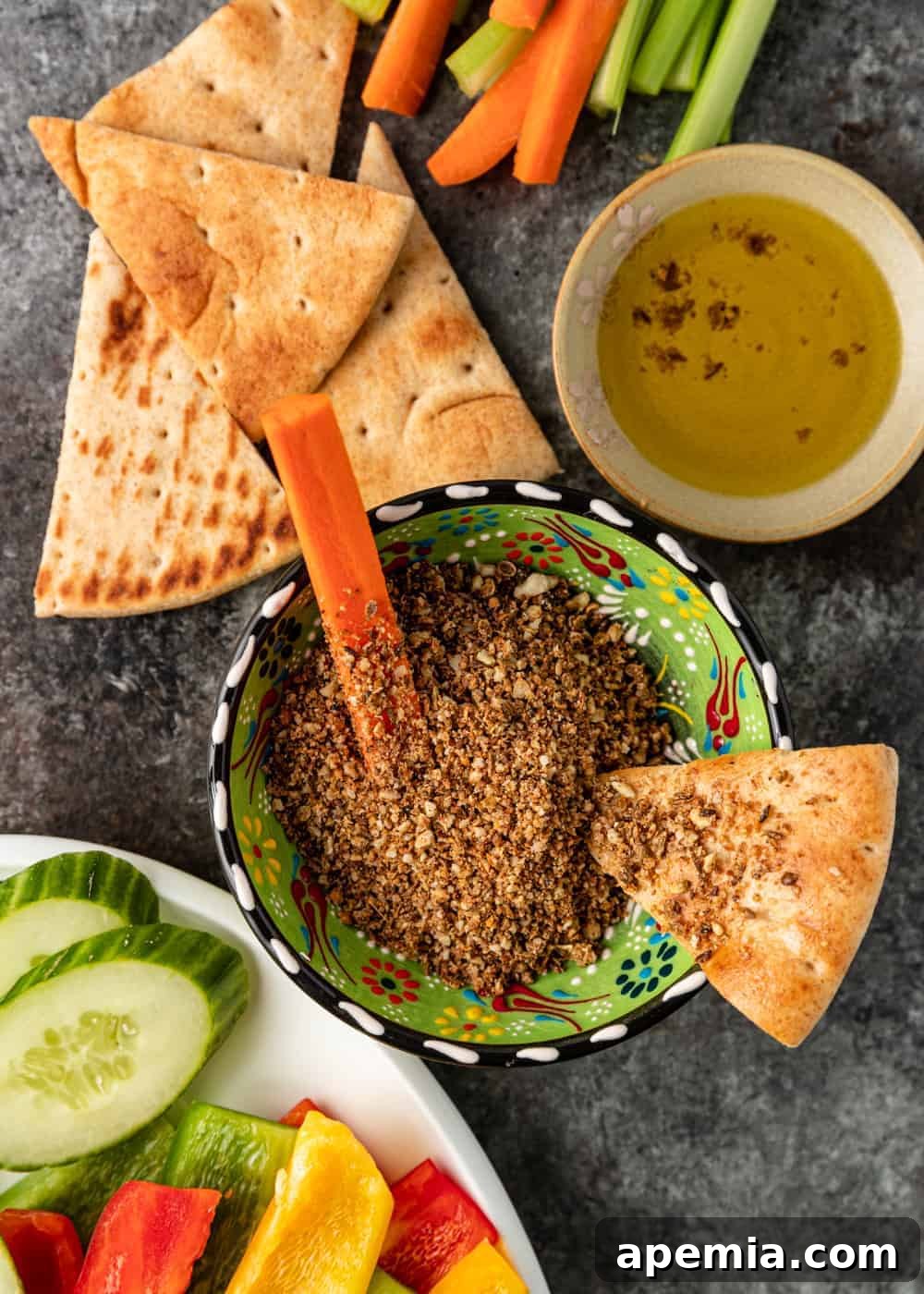 Overhead image: A green pottery bowl brimming with Egyptian dukkah, accompanied by crisp carrot sticks and a warm slice of pita bread, ready for a delightful dipping experience.