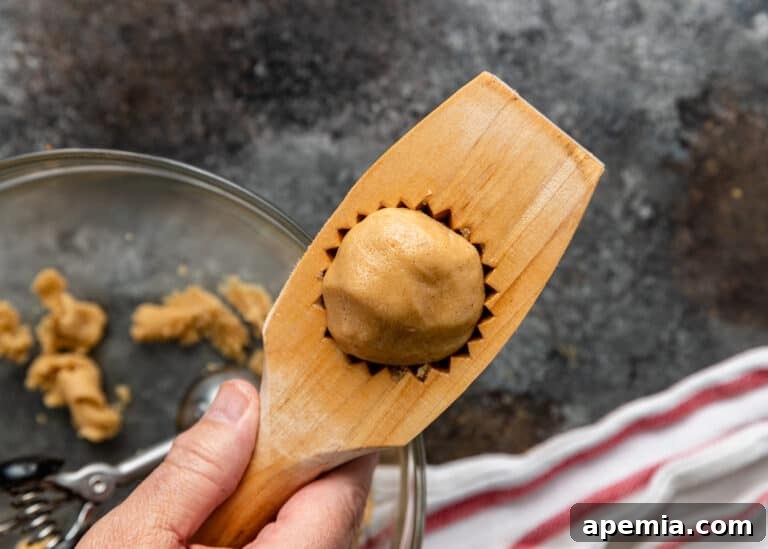 A scoop of cookie dough being pressed inside a traditional wooden maamoul mold, illustrating the shaping technique.