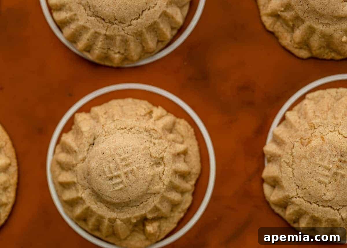 Overhead closeup of a baking sheet filled with buttery, stuffed Maamoul cookies, showcasing their golden-brown tops before powdering.