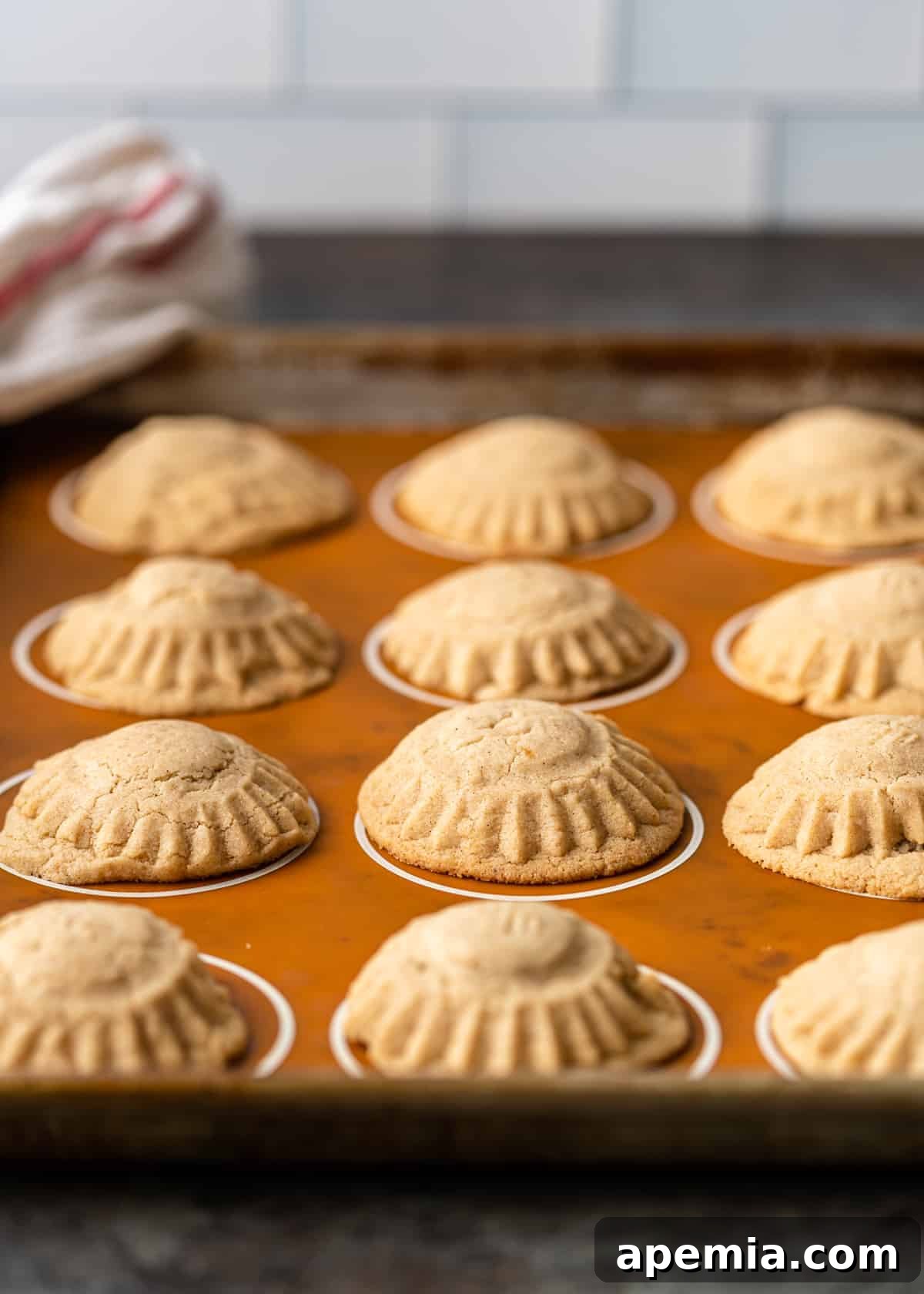 Buttery, stuffed Maamoul cookies are shown cooling on a baking pan after being removed from the oven, awaiting their final dusting of powdered sugar.