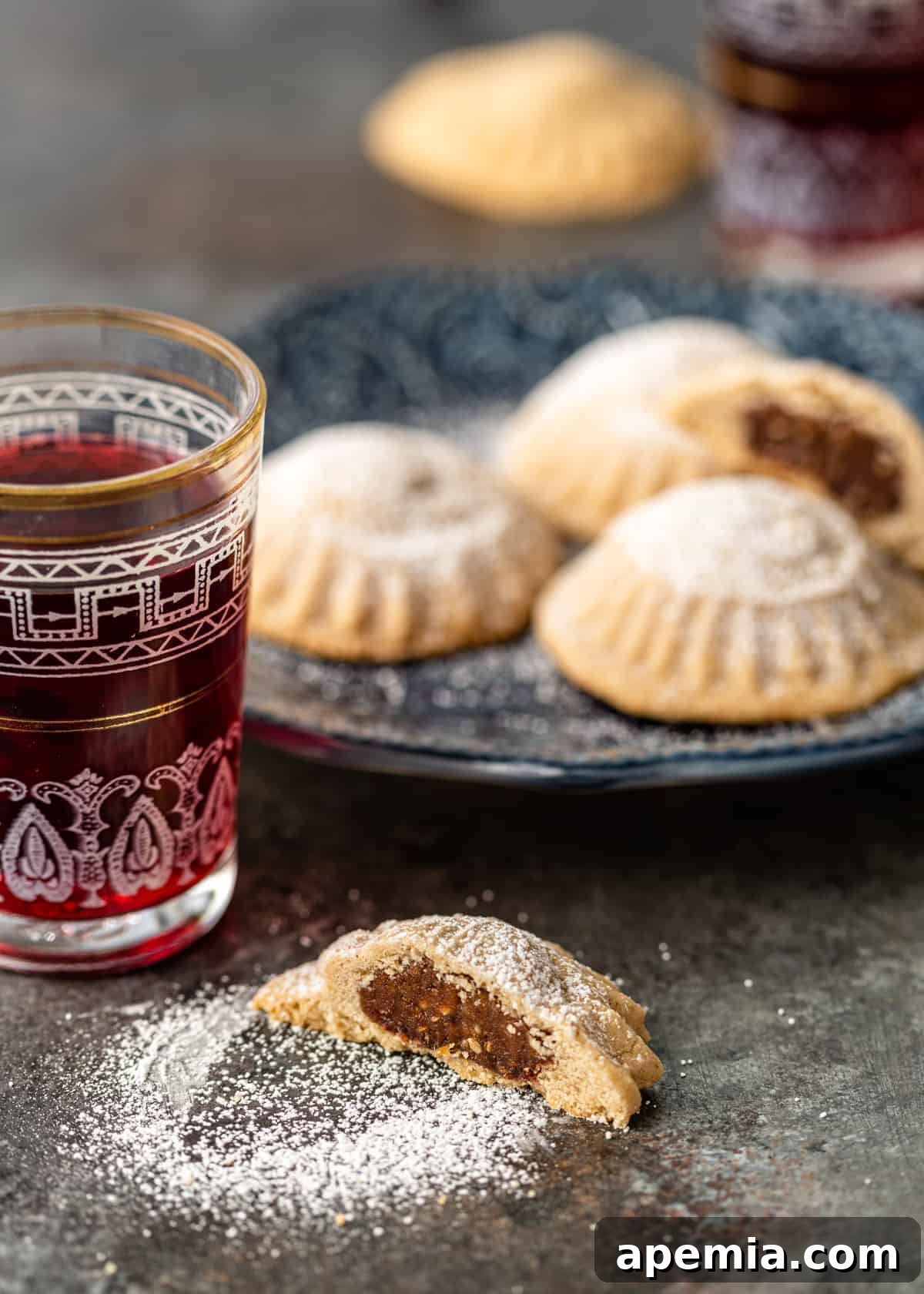 A plate of freshly baked maamoul cookies is presented alongside a refreshing glass of hibiscus tea, creating a beautiful and inviting scene.