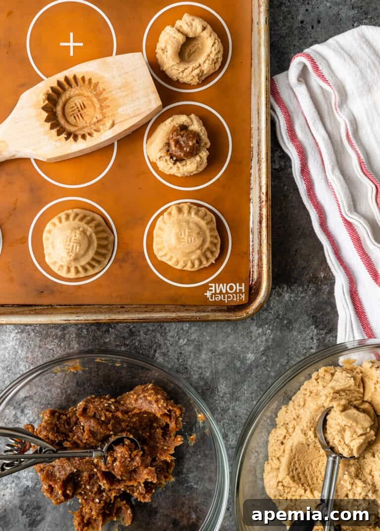 Overhead view of bowls filled with raw cookie dough and the date filling, arranged alongside a baking pan ready with molded Maamoul cookies, illustrating the preparation stage.