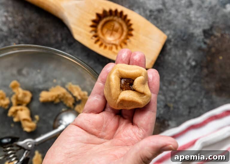The process of adding sweet fruit filling into a prepared cookie dough ball for the maamoul recipe.