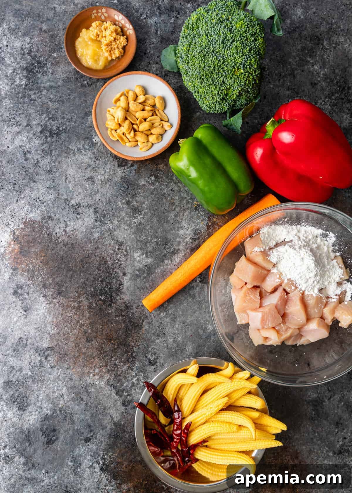 Overhead view of raw chicken breast pieces in a bowl, surrounded by bowls of stir-fry vegetables, peanuts, and ginger paste
