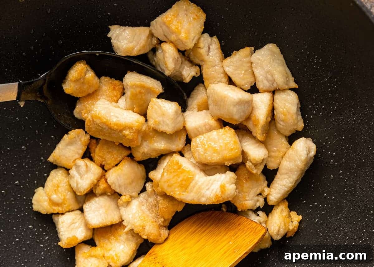 Overhead closeup of tossing chicken pieces in a wok for Hunan chicken stir-fry