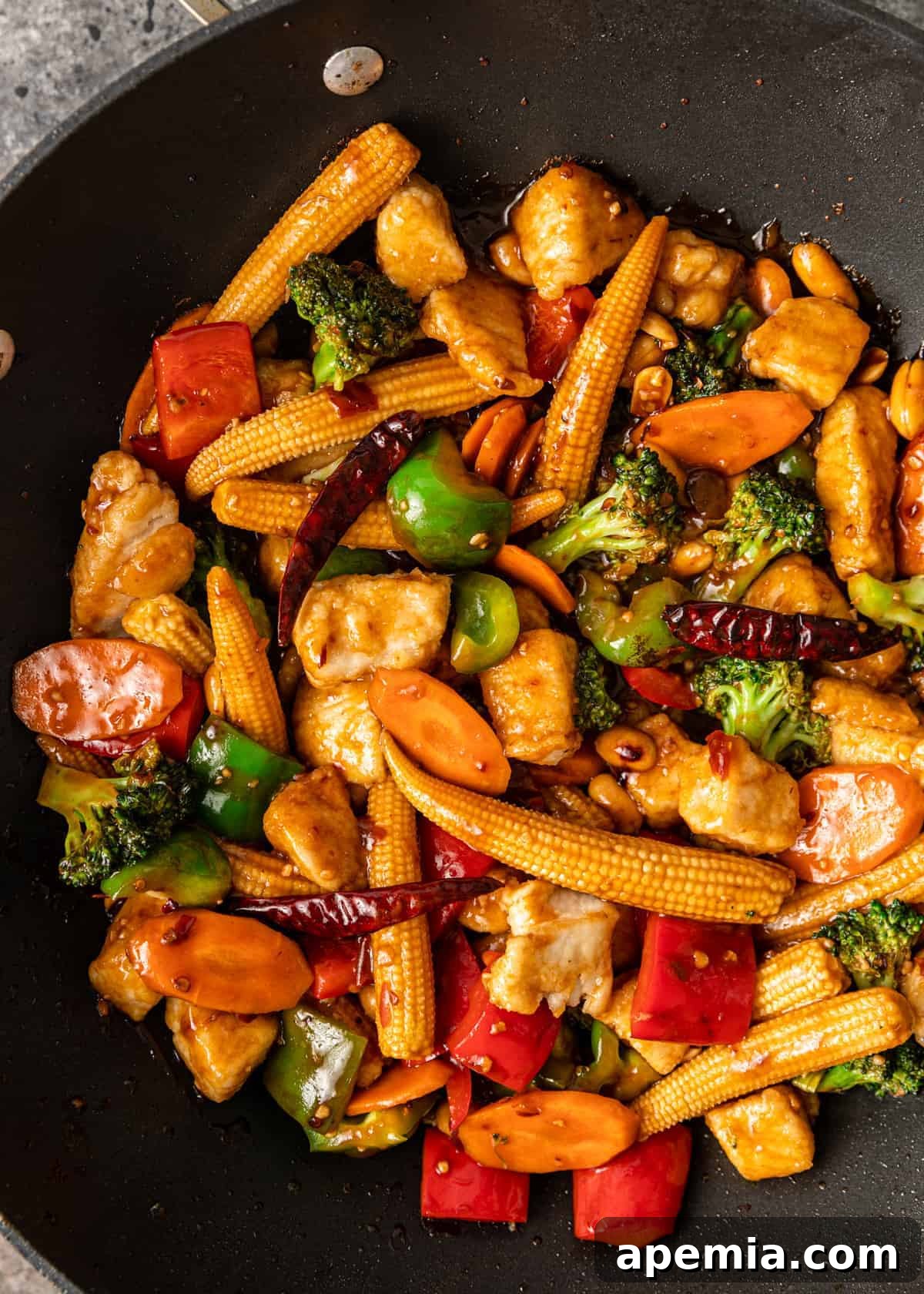 Overhead view of stir-frying meat and vegetables with Hunan sauce in a wok, showing the vibrant colors