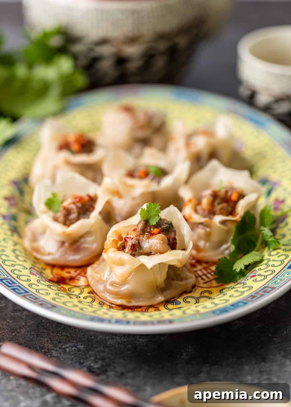 cooked shrimp shumai dumpling in sauce on an ornate blue and yellow plate with cilantro garnish
