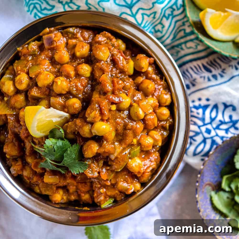 Overhead shot of a gleaming silver bowl overflowing with vibrant chickpea curry, generously garnished with fresh cilantro and a lemon wedge.