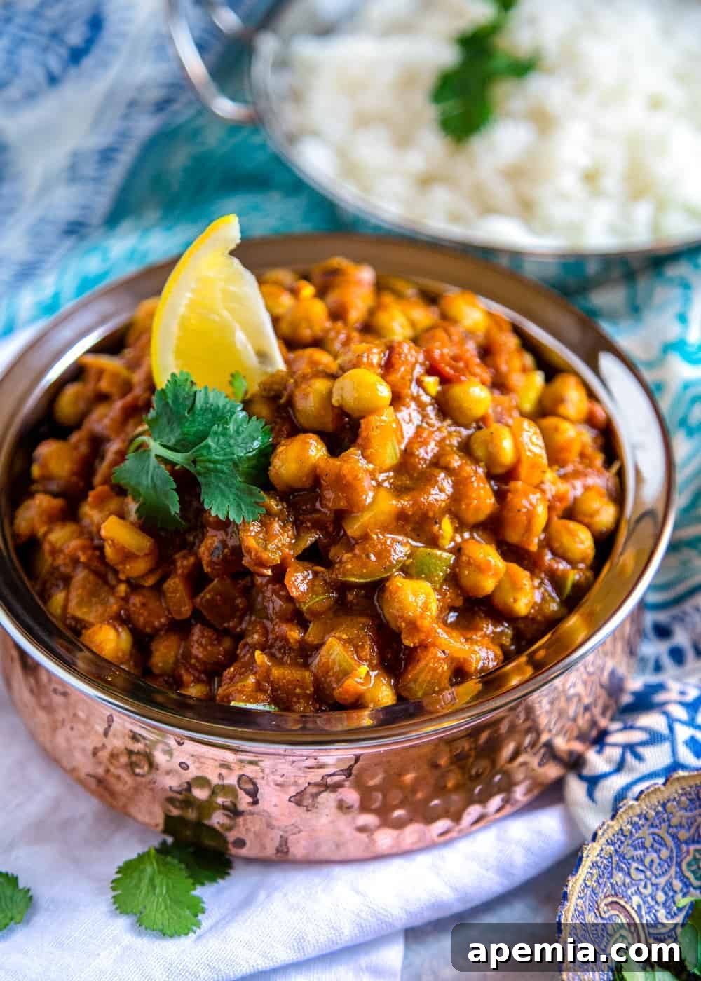 Close-up view of a generous serving of chickpea masala in a hammered steel serving bowl, highlighting the thick, rich sauce, tender chickpeas, and vibrant spice infusion.