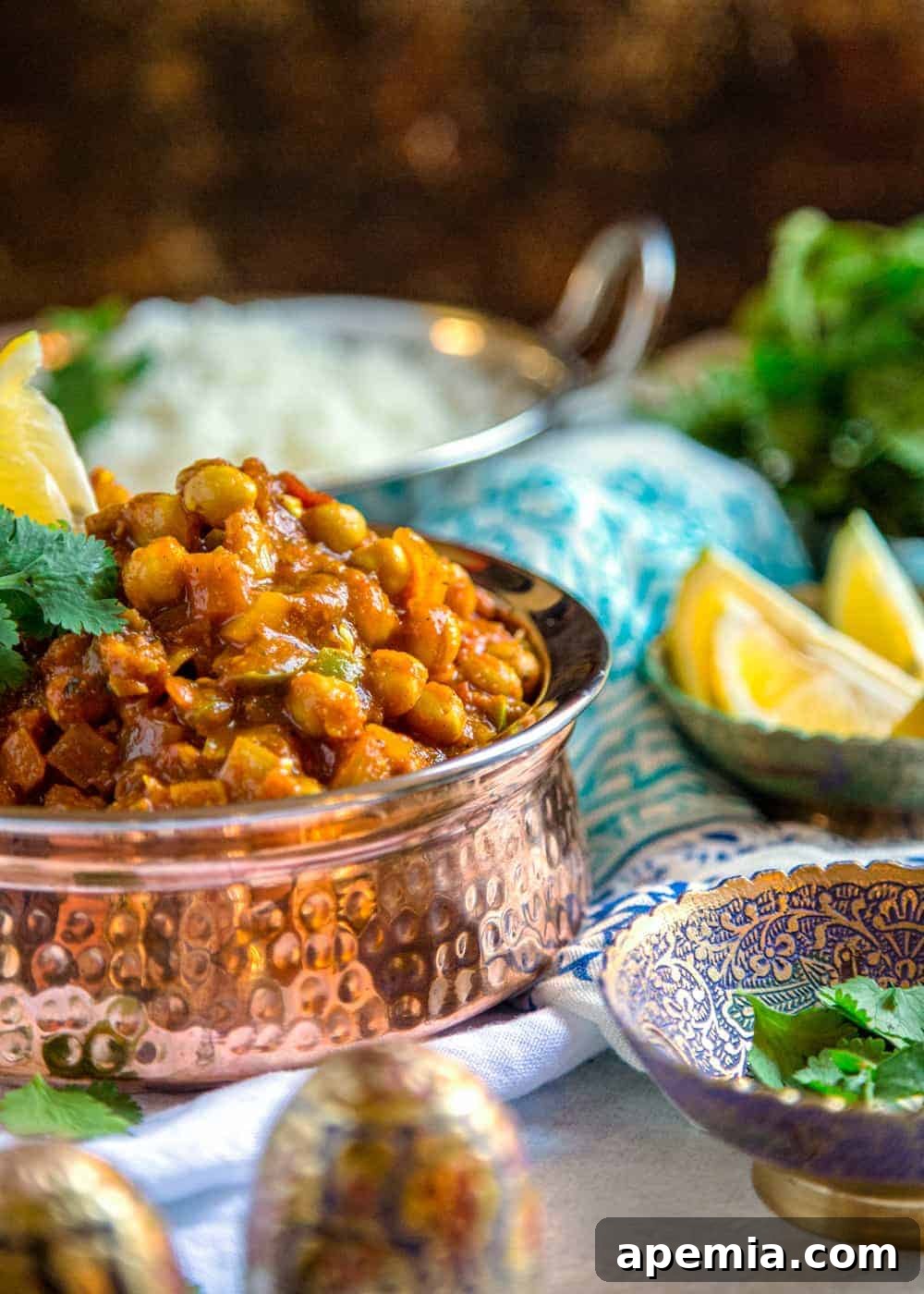 Side view of a hammered copper serving bowl filled with chickpea curry, garnished with vibrant green cilantro and a lemon wedge.