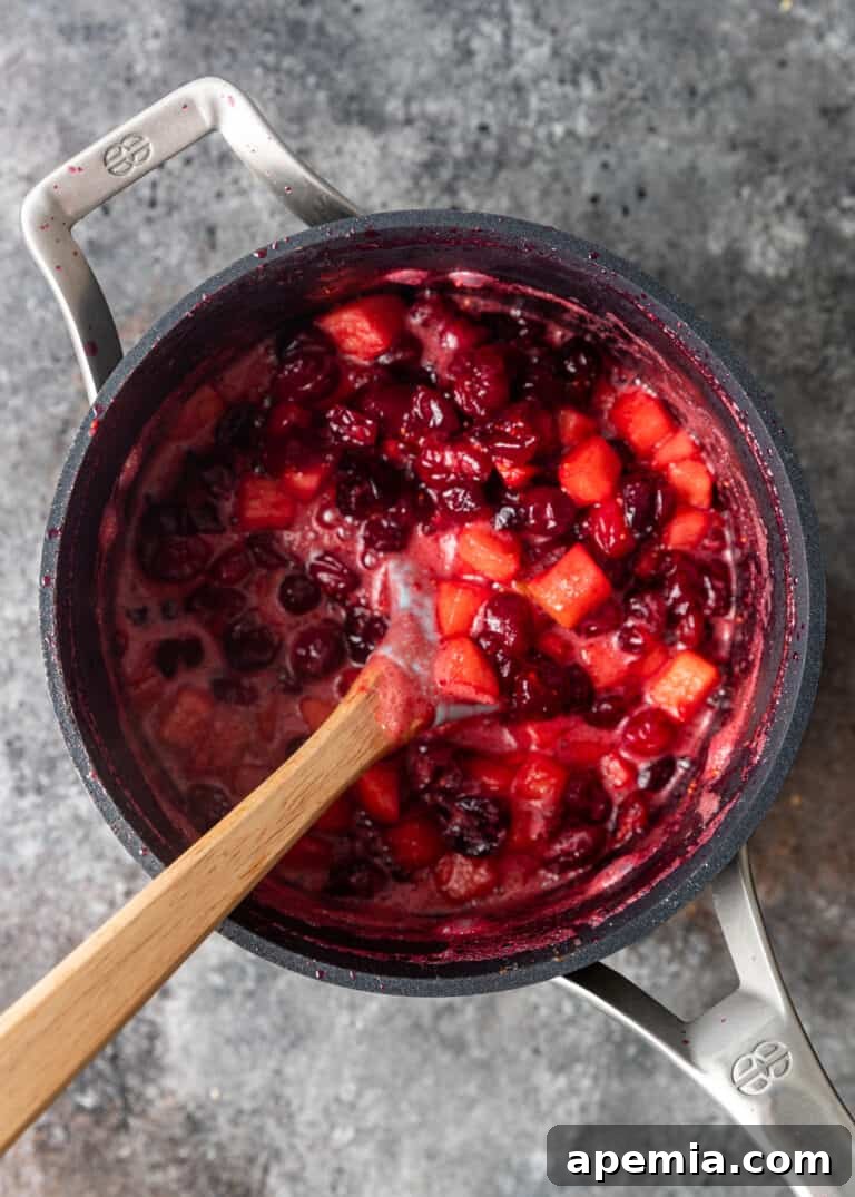 cooked cranberries and apples simmering in saucepan, beginning to thicken