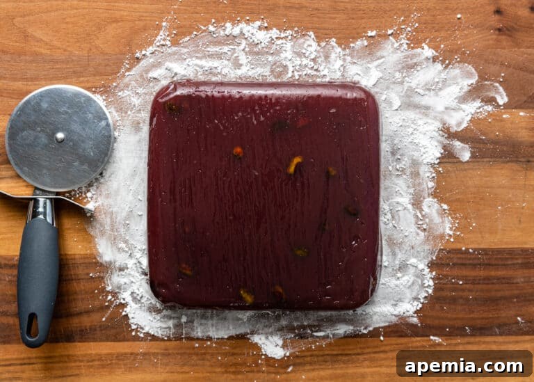 Homemade pomegranate gelatin candy on a wood cutting board after removing the parchment paper.