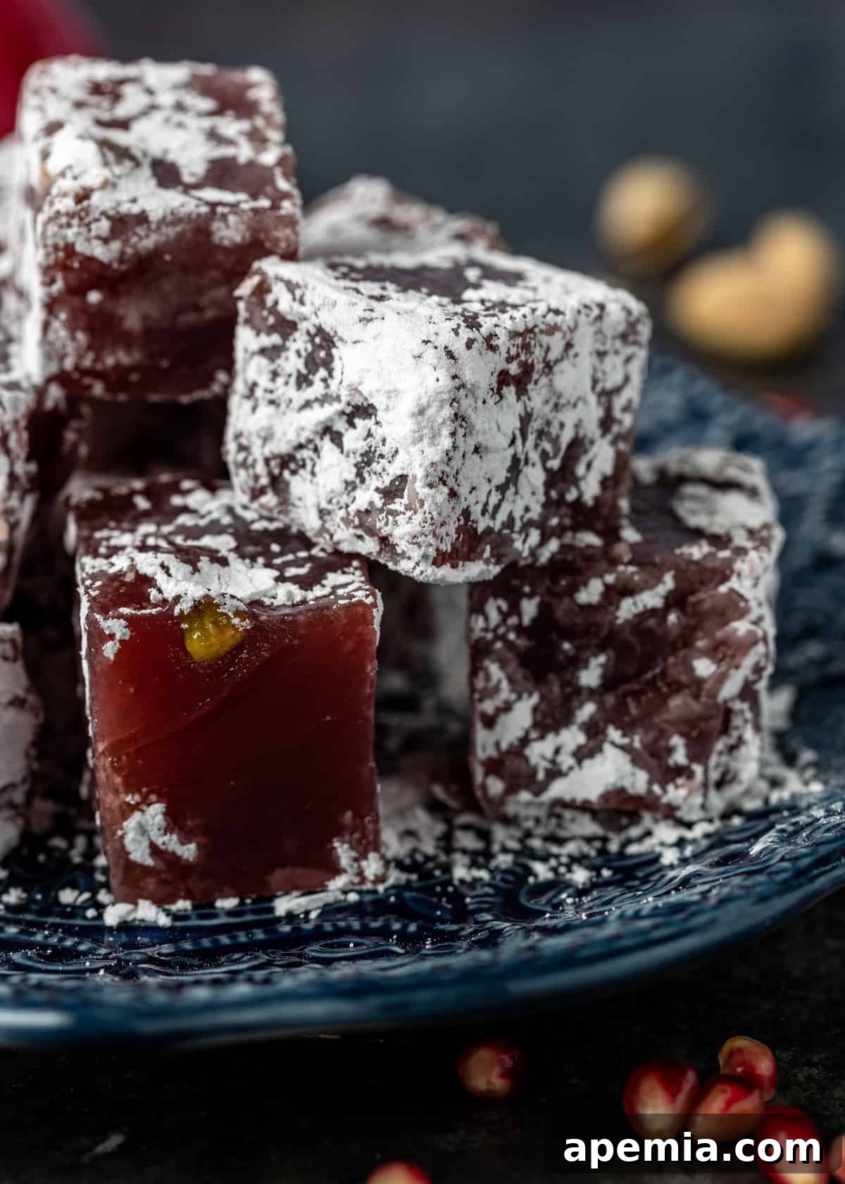 Squares of homemade pomegranate gelatin candy (Lokum) arranged elegantly on a glass plate, ready to serve.