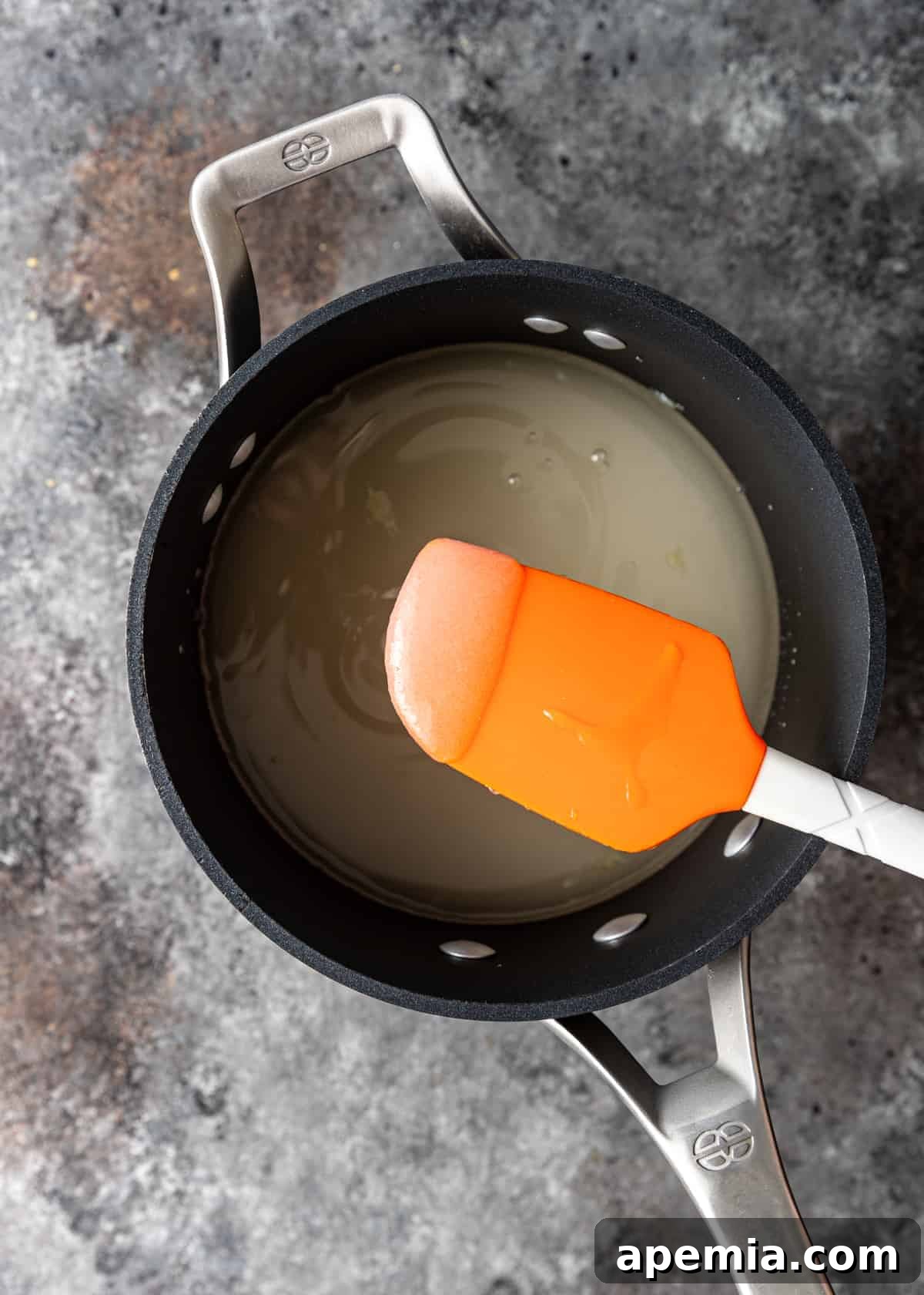 Granulated sugar melting with water in a saucepan over gentle heat.