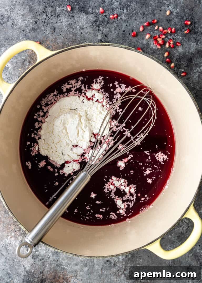 Pomegranate juice, cornstarch, and lemon juice being whisked together in a Dutch oven to form the base.