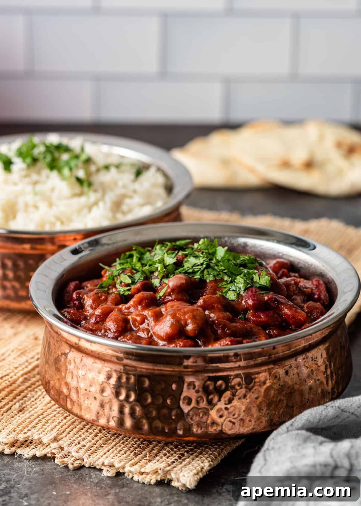A beautifully presented bowl of Rajma Chawal garnished with fresh cilantro, accompanied by a side of steamed basmati rice and warm naan bread.