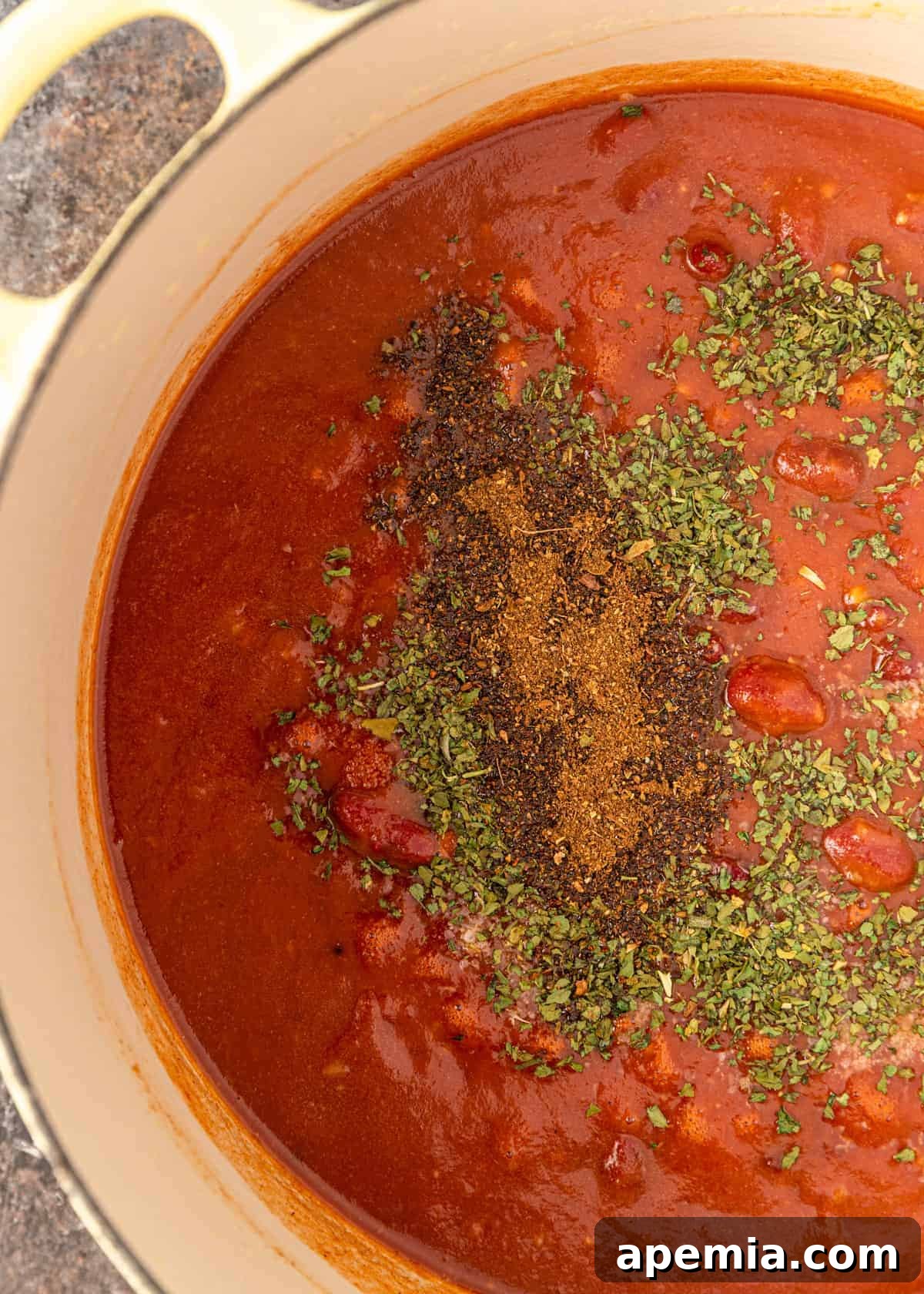 Overhead view of tomato passata, fenugreek leaves, and garam masala being added to the cooked onion base in a Dutch oven.