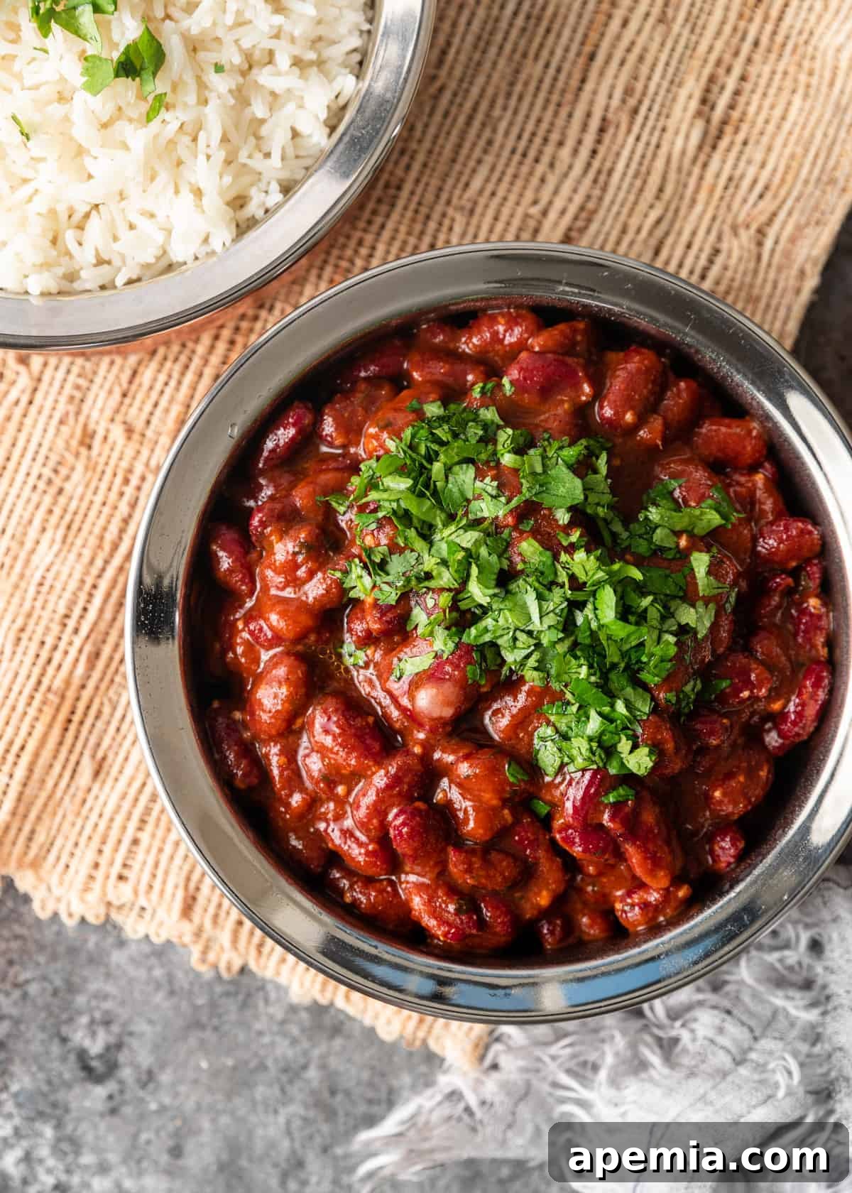 Overhead shot of a bowl of steaming Kidney Bean Curry garnished with cilantro, next to a bowl of fluffy basmati rice, ready to be served.
