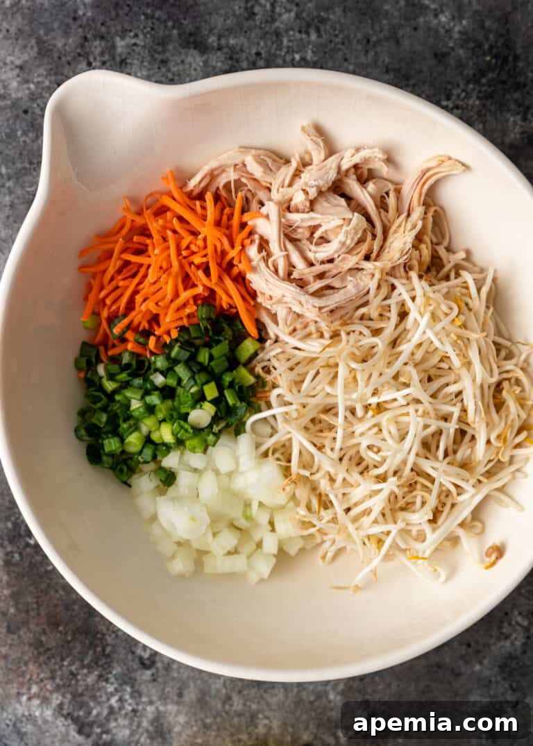 overhead process shot: shredded chicken, carrot, scallion and bean threads in white bowl