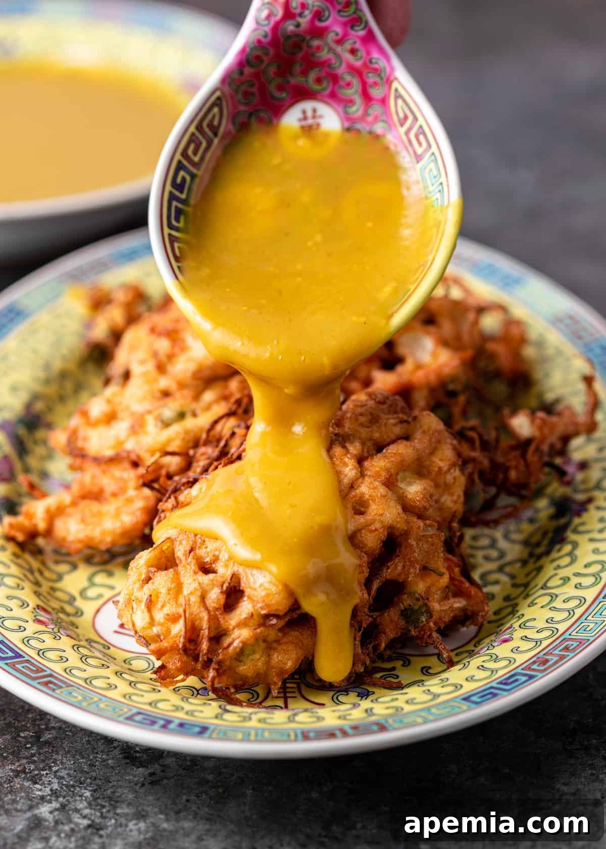 spooning yellow sauce over my egg foo young recipe on a ceramic platter