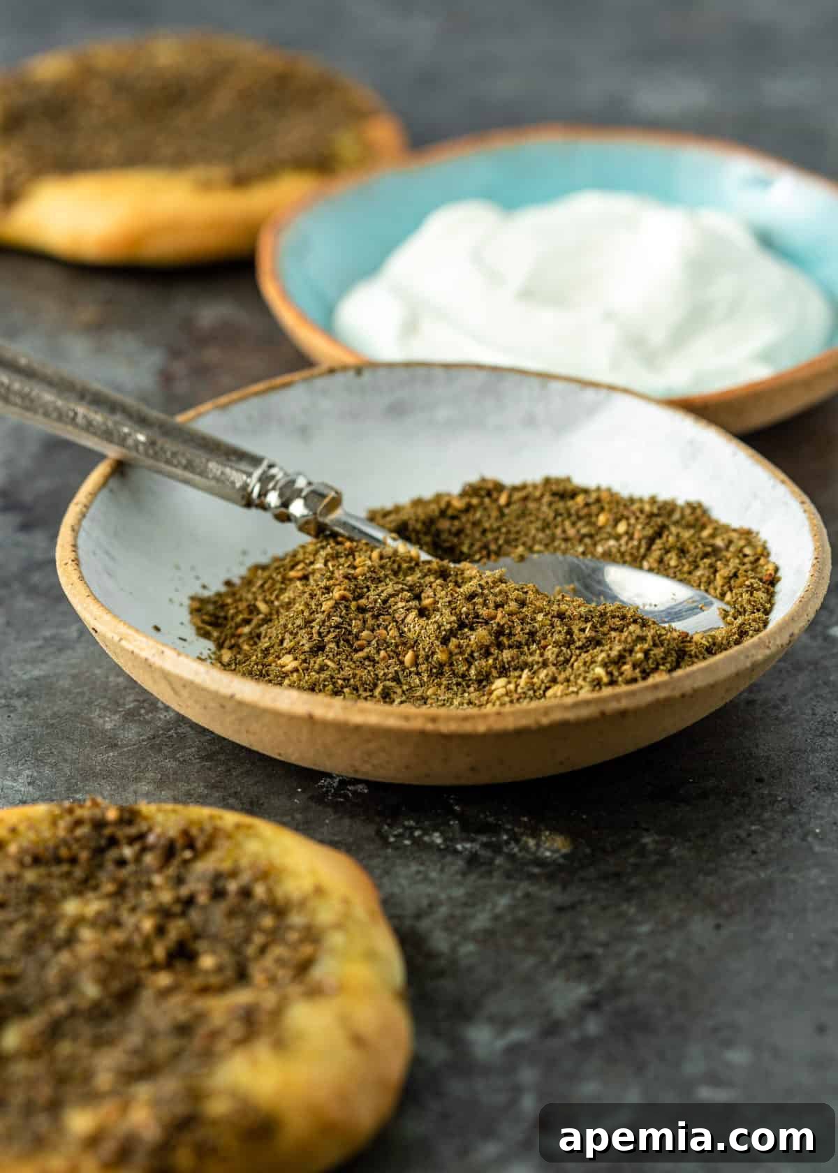 Crafting Your Own Lebanese Zaatar Blend 3 A rustic wooden spoon rests in a bowl of homemade Lebanese Za'atar spice blend, with a creamy bowl of labneh (strained yogurt) blurred in the background, suggesting a delightful pairing.