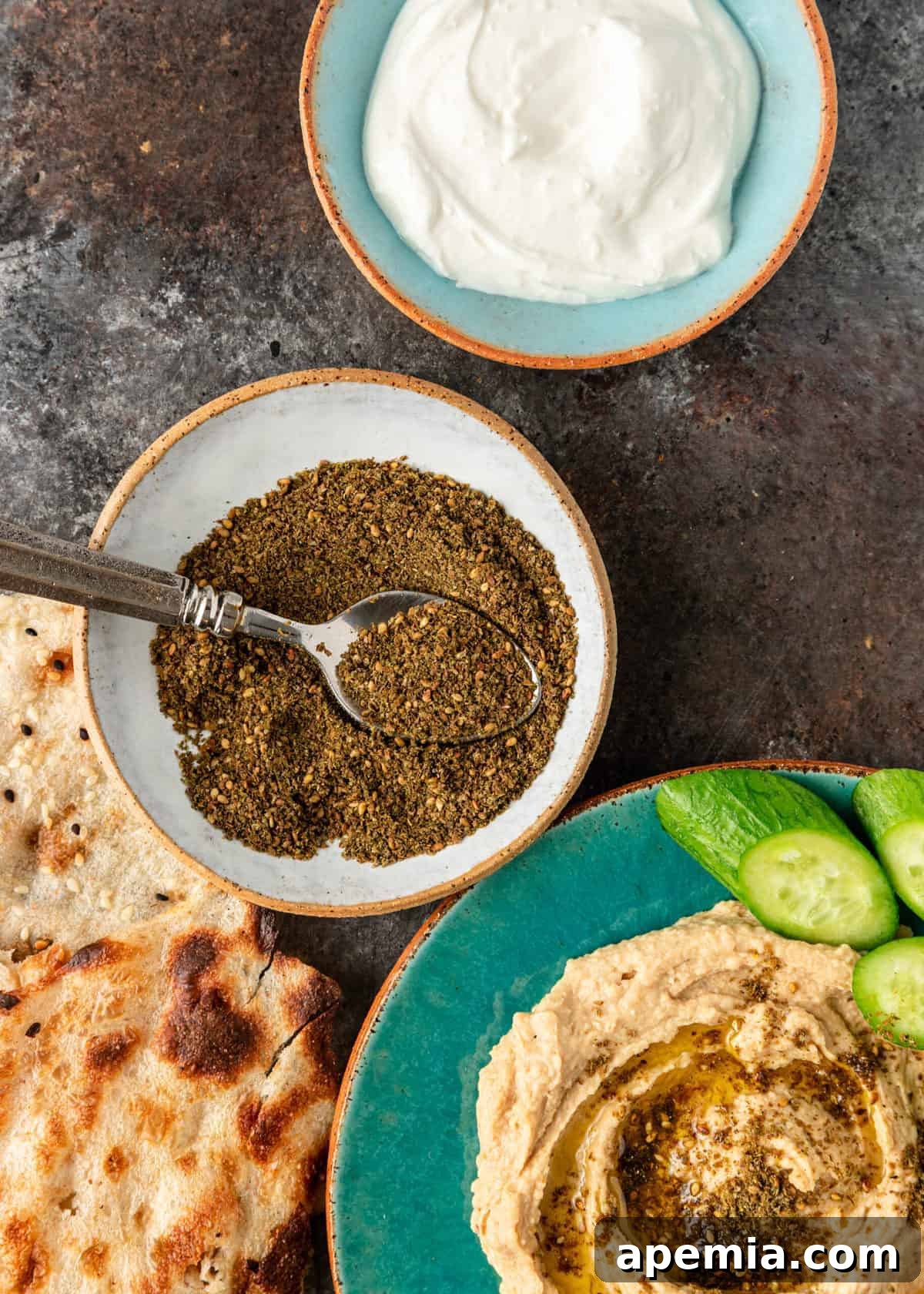 Crafting Your Own Lebanese Zaatar Blend 5 An overhead close-up view of a small bowl filled with Za'atar, surrounded by lavash bread, a bowl of creamy hummus, and a dollop of labneh, perfect for a Mediterranean spread.