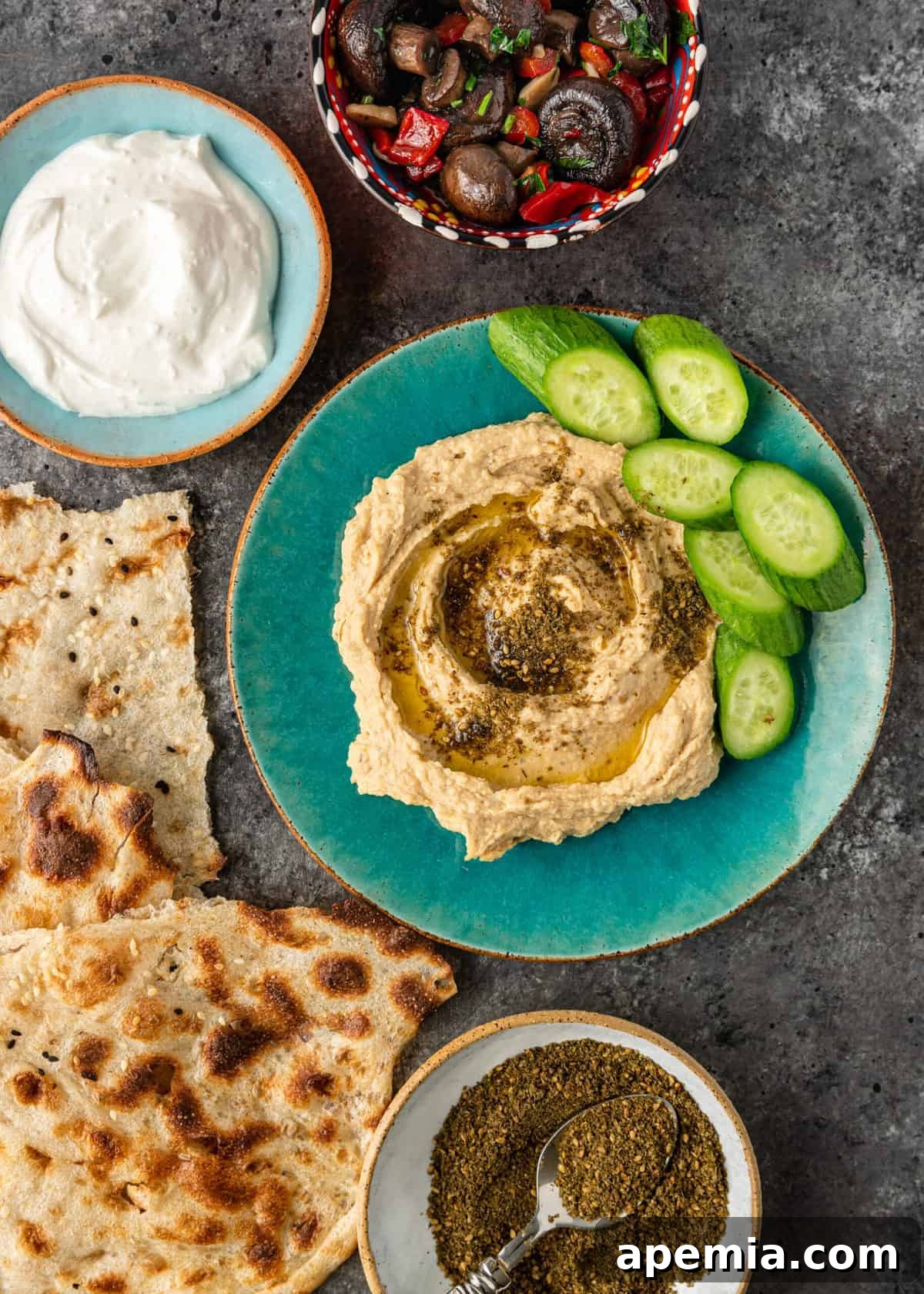 Crafting Your Own Lebanese Zaatar Blend 6 A bowl of creamy hummus generously topped with a sprinkle of Lebanese Za'atar spice blend and a side of fresh sliced cucumbers, ideal for dipping.