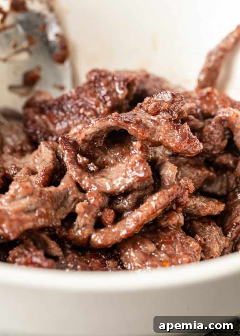 Close-up shot of perfectly stir-fried strips of beef resting in a white bowl, showcasing their tender and velvety texture.