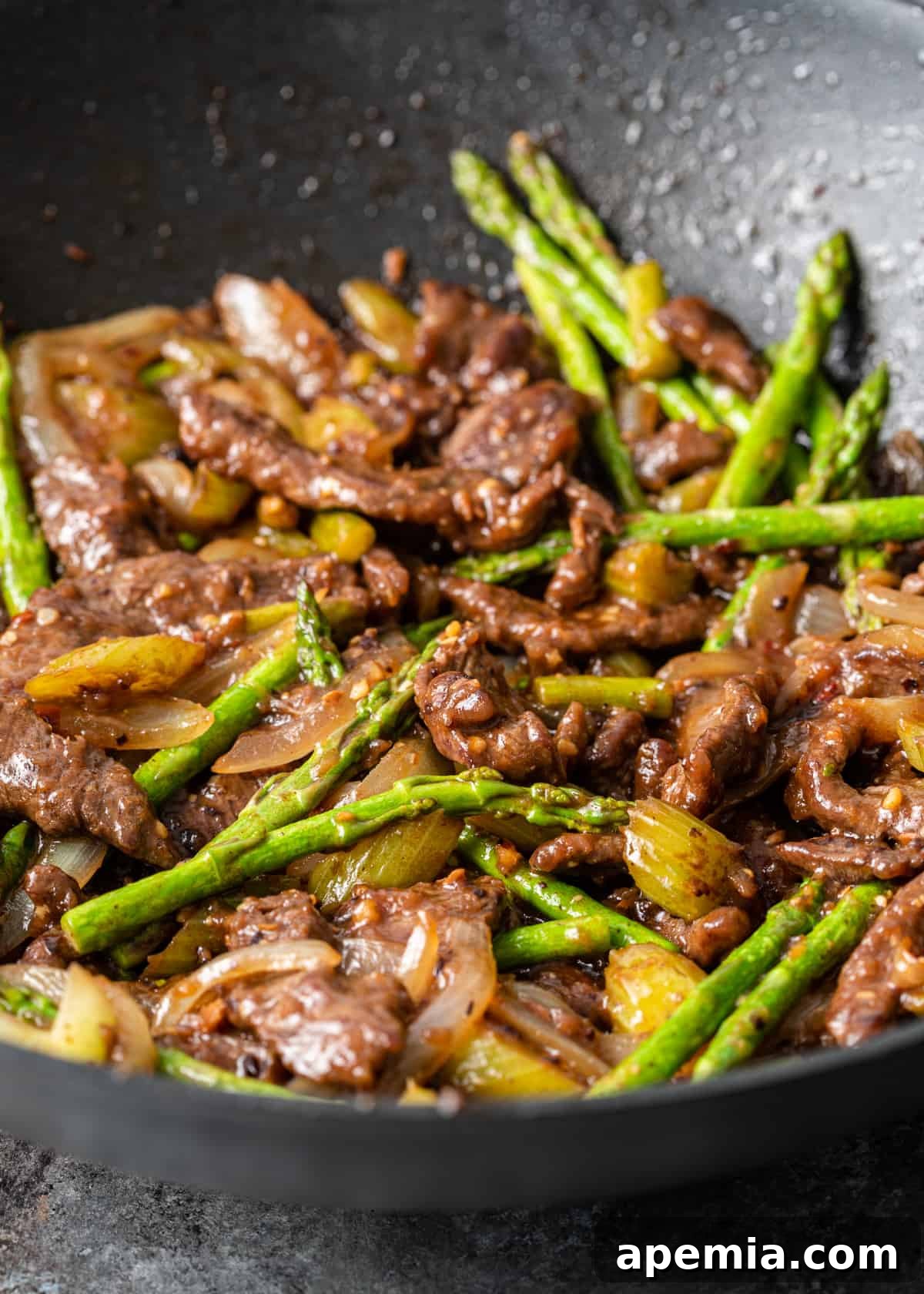 Dynamic shot of asparagus tips, sliced onions, celery, and tender strips of sirloin being actively stir-fried in a hot wok, illustrating the cooking process.